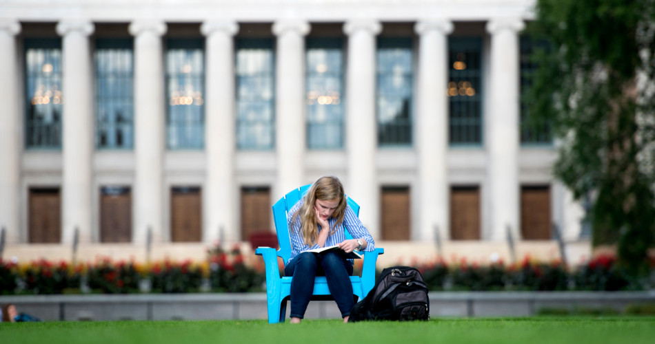 A student studies in a blue chair on the mall lawn