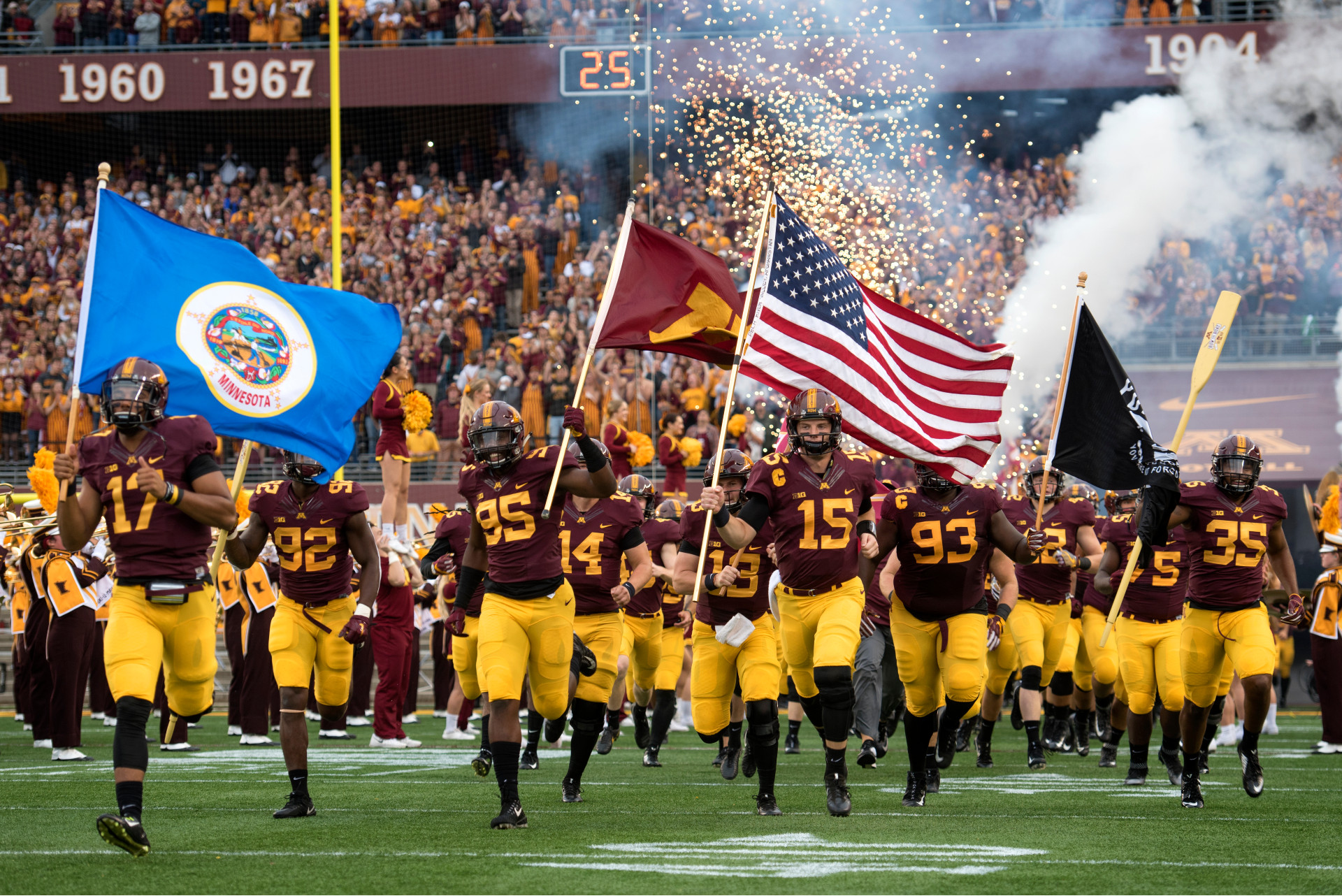 Gopher football players run onto the field on Gameday carrying the Minnesota and American flags