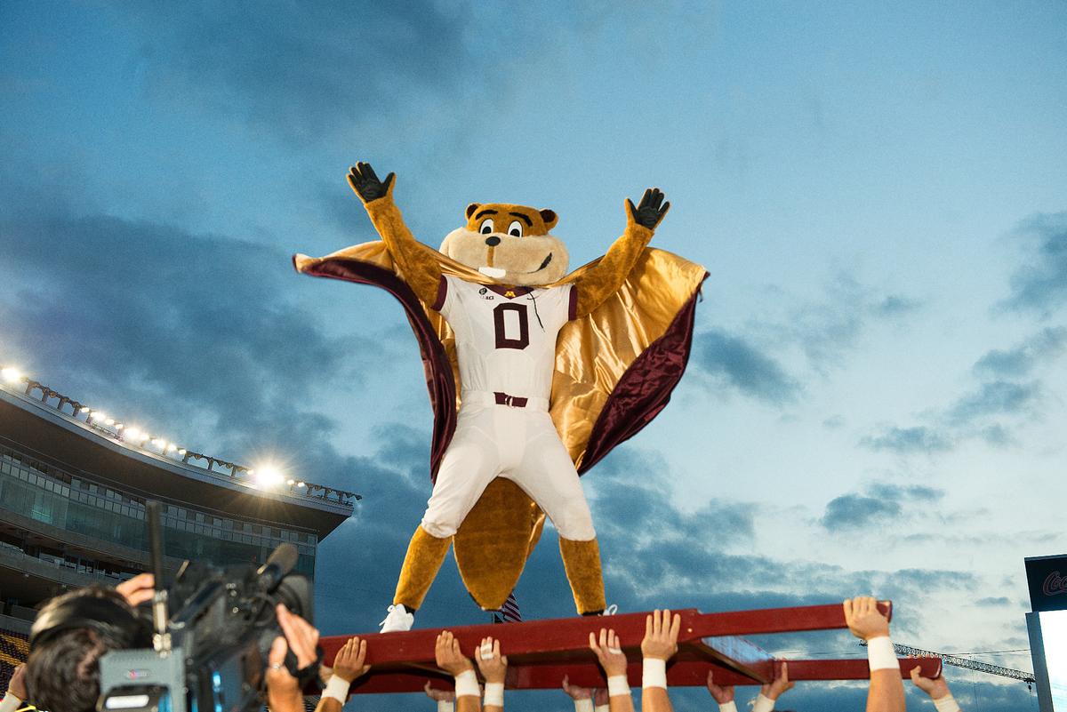 Goldy Gopher wearing a cape while standing on a platform at a football game