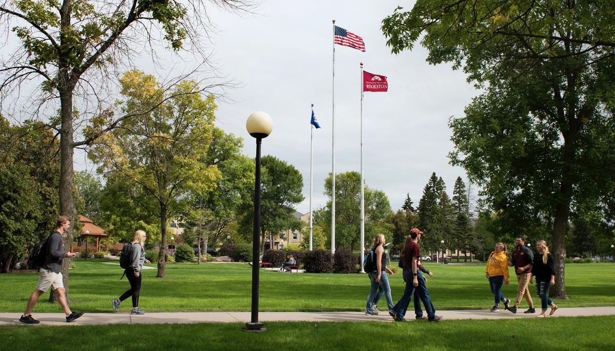 Three groups of students walking on paved path surrounded by green grass and trees on the University of Minnesota Crookston campus