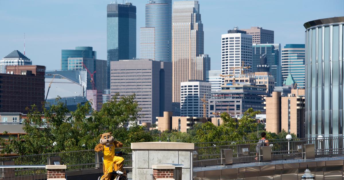 Goldy Gopher mascot giving "thumbs up" on scooter in front of Minneapolis skyline