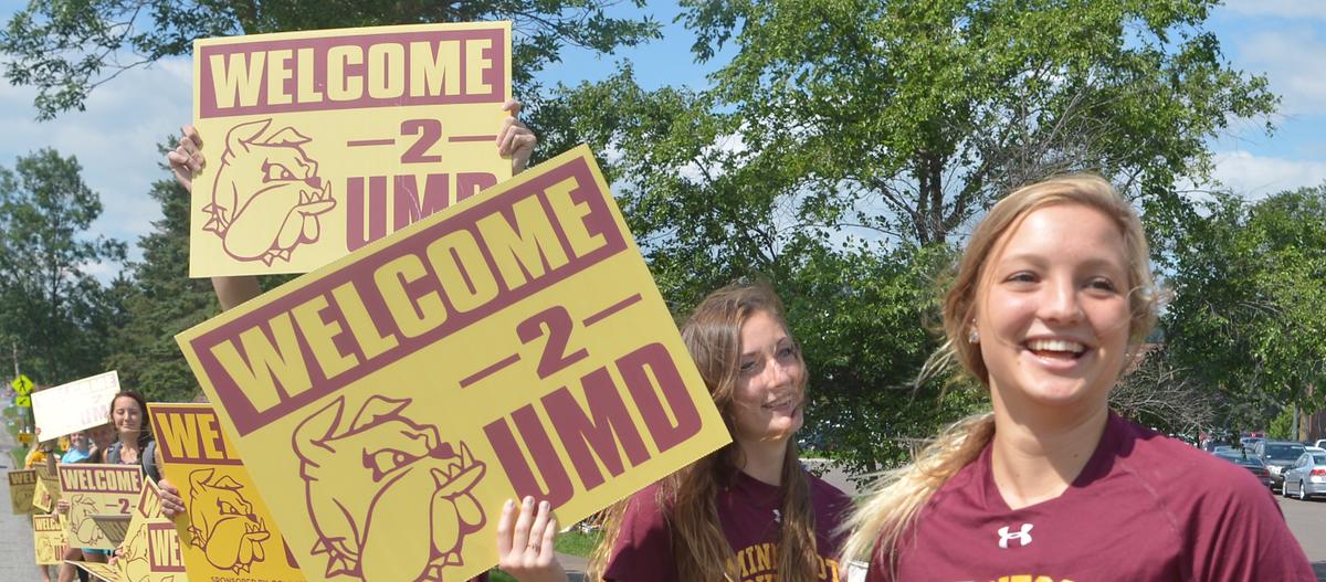 Students lined up on side of road with maroon and gold signs that say Welcome 2 UMD
