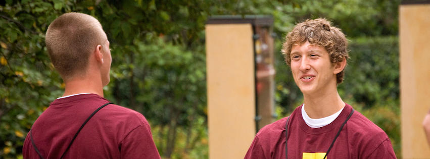 two students wearing maroon shirts chatting on campus